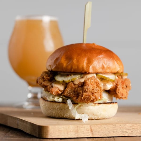 Ox Kitchen's crispy fried chicken sandwich with pickles and sauce, next to a glass of beer.