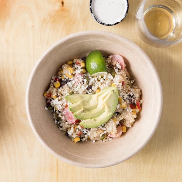 Overhead view of a quinoa bowl with avocado, corn, and cheese, next to a drink.